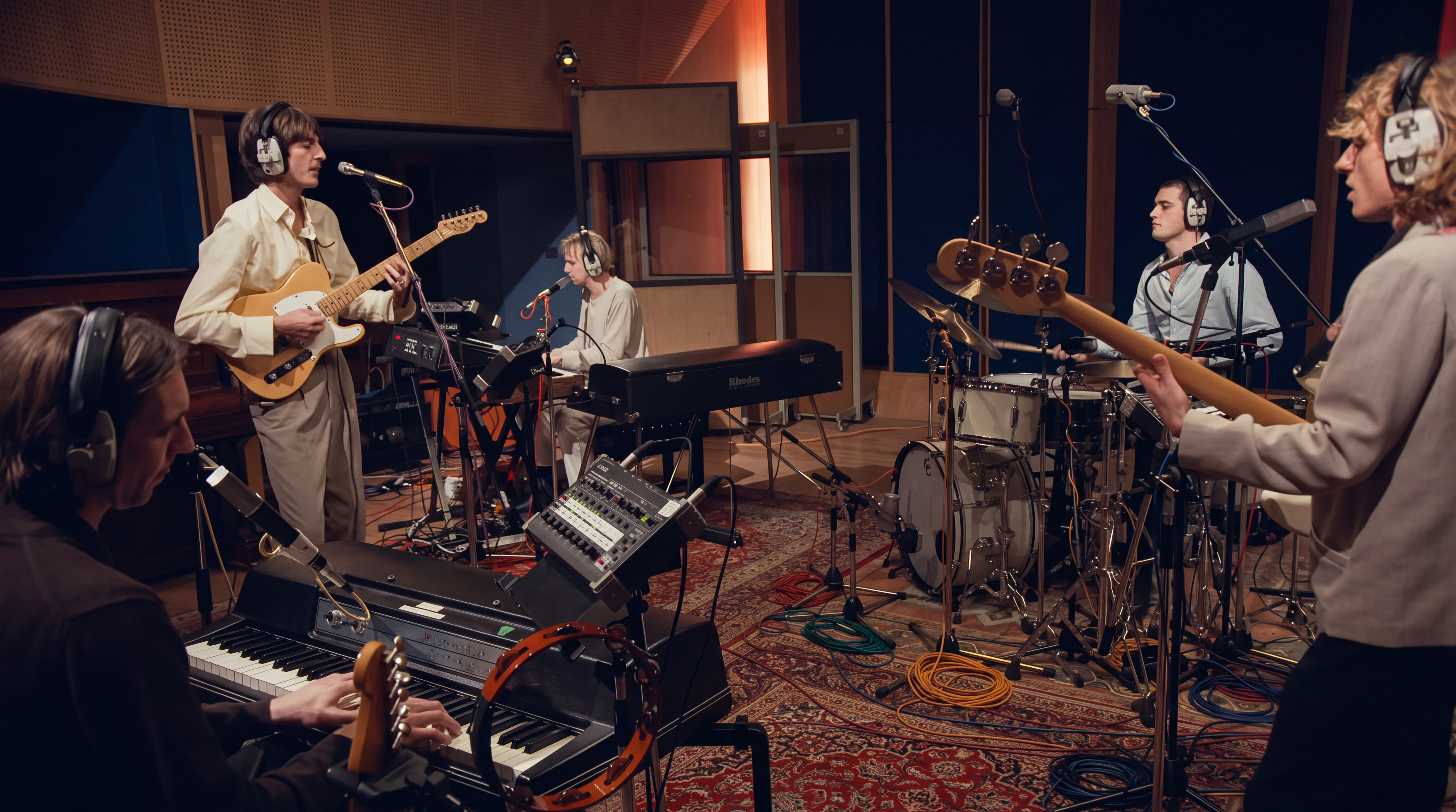 Musicians recording together in a studio, surrounded by guitars, keyboards, drums and microphones.
